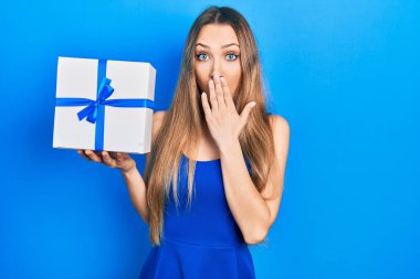 Sarışın genç kız elinde hediyeyle ağzını eliyle kapatıyor. Şok olmuş ve hata yapmaktan korkuyor. şaşırmış ifade 