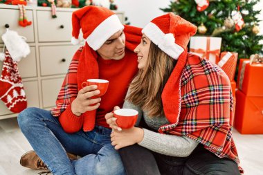 Battaniyeli Noel şapkası takan genç bir çift. Yerde oturup evde kahve içmek..