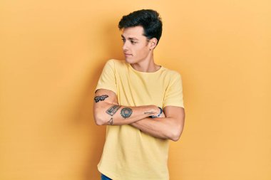 Sarı bir tişört giyen İspanyol genç adam kollarını kavuşturmuş ve kendinden emin bir şekilde yan tarafa bakıyor. 