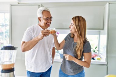 Orta yaşlı İspanyol çift gülümsüyor. Mutfakta bir bardak smoothie içiyorlar..