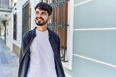 Genç İspanyol adam gülümseyerek şehirde mutlu mesut dikiliyor..