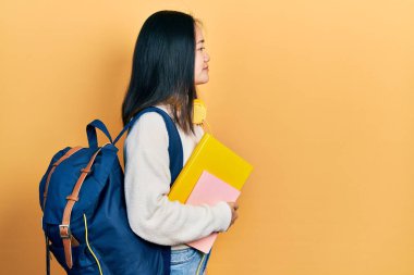 Sırt çantası ve kitap tutan genç Çinli kız, rahat profil pozu, doğal bir yüz ve kendine güvenen bir gülümseme.. 