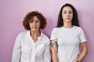İspanyol anne ve kızı pembe arka plan üzerine gündelik beyaz tişört giyiyorlar. Uykulu ve yorgun görünüyorlar. Yorgunluktan ve akşamdan kalmalıktan bitkinler.. 