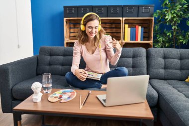 Young beautiful woman practicing painting looking at online tutorial pointing finger to one self smiling happy and proud 