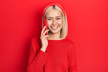 Güzel sarışın kadın akıllı telefondan konuşuyor. Olumlu ve mutlu görünüyor. Kendine güvenen bir gülümsemeyle dişlerini gösteriyor. 