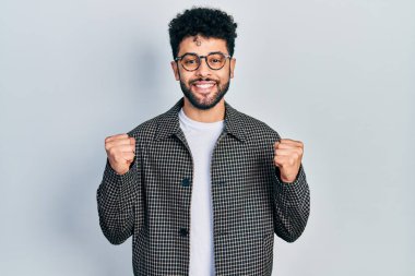 Sakallı, gözlüklü genç bir Arap, kolları açık ve gözleri açık bir şekilde başarıyı kutluyor ve şaşırıyor. Kazanan konsept. 