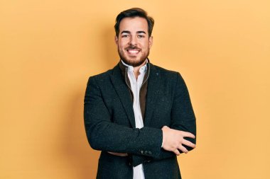 Sakallı, zarif iş ceketi giyen, kollarını kavuşturup kameraya gülümseyen yakışıklı beyaz adam. pozitif kişi. 