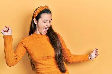 Young brunette teenager wearing casual yellow sweater dancing happy and cheerful, smiling moving casual and confident listening to music 