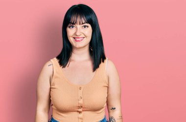 Genç, İspanyol asıllı, iri yarı, mutlu ve havalı bir gülümsemesi olan sıradan kıyafetler giyen bir kadın. şanslı kişi. 