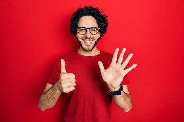 Yakışıklı İspanyol gömlekli ve gözlüklü adam 6 numaralı parmaklarını gösterip gösterirken kendinden emin ve mutlu gülümsüyor.. 