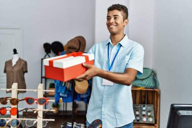 Young hispanic man working as shop assistant selling gift at retail shop
