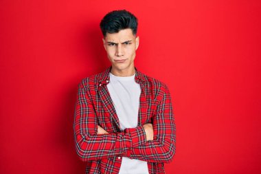 Gündelik kıyafetler giyen, kuşkucu ve gergin genç İspanyol bir adam. Yüzünde çapraz kollarla onaylamayan bir ifade var. negatif kişi. 