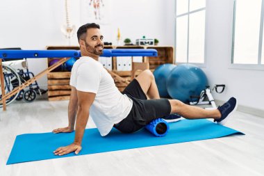 Genç İspanyol hasta gülümsüyor. Bacak rehabilitasyonu seansı için klinikte köpük rulo kullanıyor.