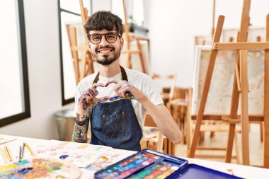 Sanat stüdyosunda sakallı bir İspanyol aşık gülümseyip elleriyle kalp sembolü çiziyor. romantik kavram. 
