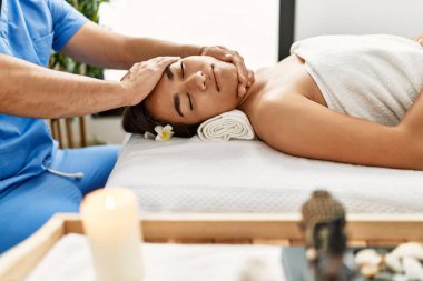 Latin erkek ve kadın fizyoterapi üniforması giyip güzellik merkezinde masaj yapıyorlar.