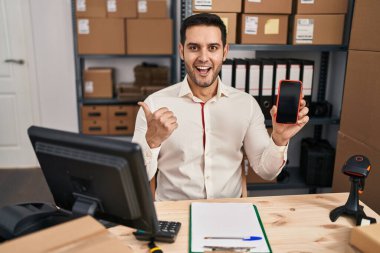 Sakallı, küçük işletmelerde çalışan, akıllı telefon ekranı gösteren, ağzı açık gülümseyen genç İspanyol bir adam. 