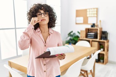 Orta Doğulu genç bir kadın ofis ağzında iş elbisesi giyiyor ve dudakları parmaklarıyla kapalı. gizli ve sessiz, tabu konuşması 