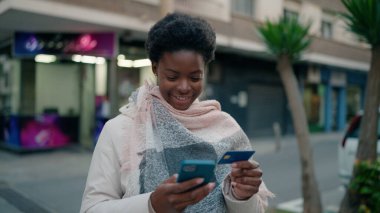 Genç Afrikalı Amerikalı kadın akıllı telefon ve kredi kartı kullanıyor.