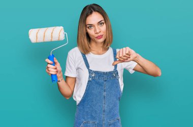 Kızgın yüzlü, paten boyacısı tutan genç sarışın kız. Eksi işareti, baş parmakları aşağıda, reddedilme konsepti. 