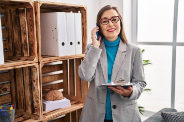 Middle age woman psychologist talking on the smartphone reading document at psychology center