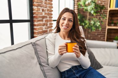 Genç İspanyol kadın evdeki kanepede kahve içiyor.