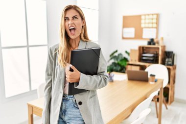 Blonde business woman at the office angry and mad screaming frustrated and furious, shouting with anger. rage and aggressive concept. 