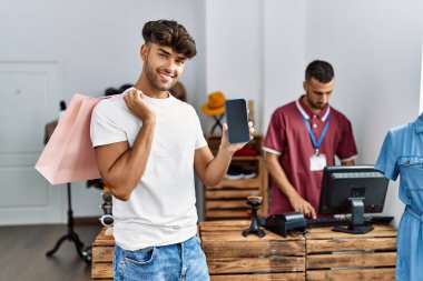 Genç İspanyol müşteri alışveriş çantası ve akıllı telefonu giyim mağazasında tutuyor..