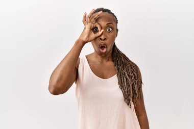 Saçları örgülü siyah bir kadın izole edilmiş arka planda duruyor. Şaşırmış bir yüz ve parmaklarından bakan bir gözle şaşırmış bir jest yapıyor. İnançsız ifade. 