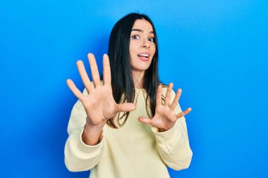 Genç esmer kadın, günlük kazak giyiyor korku ifadesinden korkuyor ve dehşete düşüyor. El kol hareketi yapmayı kes, şok içinde bağırmayı kes. panik konsepti. 