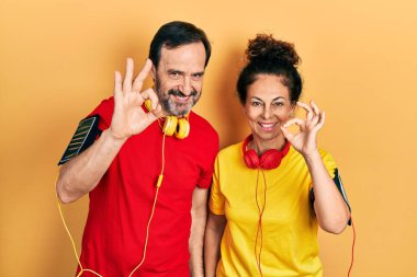 Orta yaşlı bir çift İspanyol kadın ve spor giysisi ve kolluk takan adam gülümsüyor ve el ve parmaklarıyla imza atıyorlar. başarılı ifade. 