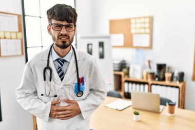 Sakallı, doktor üniforması giyen ve midesi üstünde steteskop kullanan İspanyol bir adam. Çünkü hazımsızlık, acı verici bir hastalık ve kendini iyi hissetmiyor. Ağrı kavramı. 