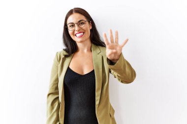 Genç esmer kadın izole edilmiş arka planda duruyor ve dört numarayı gösterip işaret ederken kendinden emin ve mutlu bir şekilde gülümsüyor.. 
