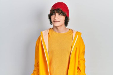 Sarı yağmurluk giyen yakışıklı genç adam yüzünde gülümsemeyle yan yana bakıyor, doğal bir ifade. Kendinden emin gülen. 