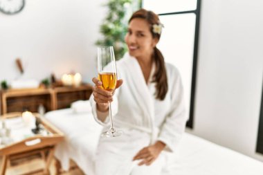 Bornoz giymiş, şampanya içen genç Latin kadın. 