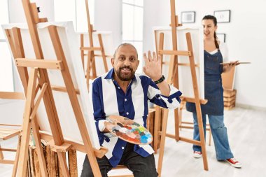 Sanat stüdyosundaki kıdemli sanatçı merhaba diyor mutlu ve gülümseyen, dostça karşılama jesti 