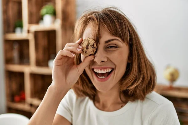 Ung Kaukasisk Kvinna Håller Kaka Över Ögat Sitter Bordet Hemma — Stockfoto