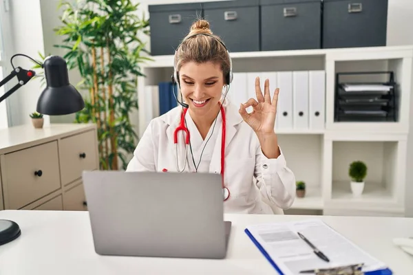 穿着医生制服的年轻女医生用笔记本电脑工作时 用手指做着确定的手势 微笑着表示友善的手势 展示着优秀的标志 — 图库照片