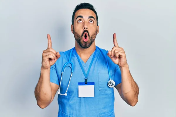Snygg Latinamerikansk Man Med Skägg Klädd Läkare Uniform Förvånad Och — Stockfoto