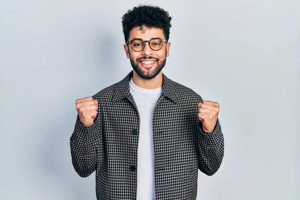 Sakallı, gözlüklü genç bir Arap, kolları açık ve gözleri açık bir şekilde başarıyı kutluyor ve şaşırıyor. Kazanan konsept. 