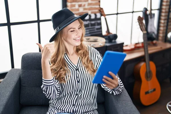 Müzik stüdyosundaki güzel sarışın kadın tablet kullanarak baş parmağını yana kaldırıyor ve ağzı açık gülümsüyor. 