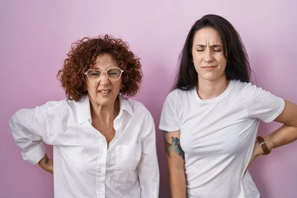 ヒスパニック系の母親と娘身に着けていますカジュアルな白いTシャツ上のピンクの背景苦しみの腰痛 手で背中に触れる 筋肉痛 — ストック写真