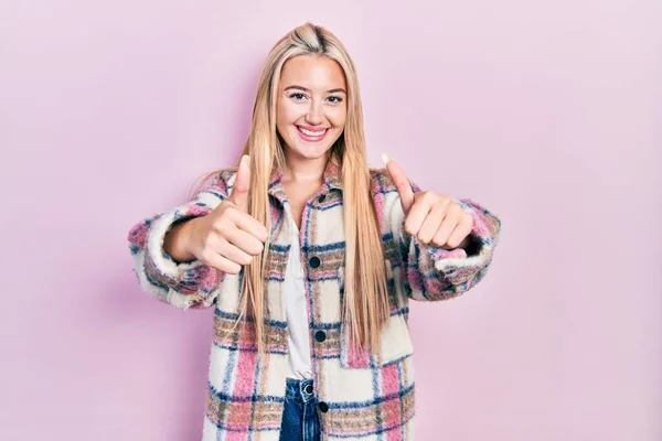 Young blonde girl wearing casual clothes approving doing positive gesture with hand, thumbs up smiling and happy for success. winner gesture.