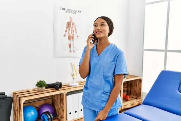 Fizyoterapist Üniforması Giyen Genç Latin Kadın Klinikte Akıllı Telefondan Konuşuyor — Stok fotoğraf