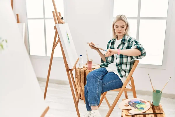 在艺术工作室的画布上 年轻的艺术家妇女正在检查腕表上的时间 放松而自信 — 图库照片