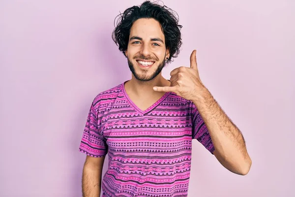 英俊的惊慌失措的男人穿着休闲的粉色T恤 微笑着用手和手指做电话手势 就像在电话里说话一样 交流概念 — 图库照片