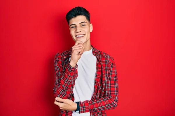 Young hispanic man wearing casual clothes looking confident at the camera with smile with crossed arms and hand raised on chin. thinking positive.