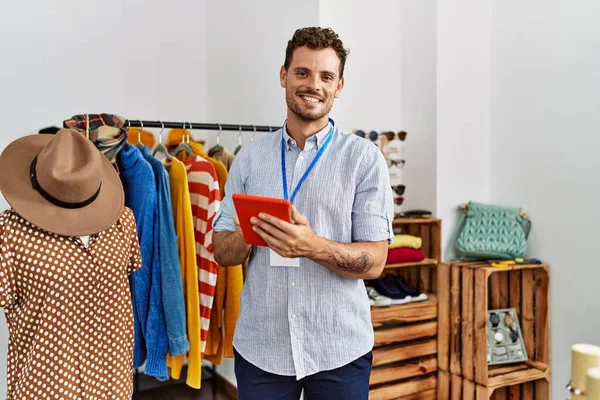 Young hispanic shopkeeper man smiling happy using touchpad working at clothing store.