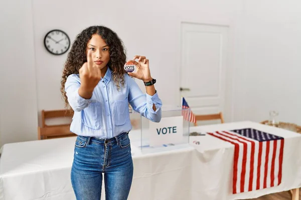 Beautiful hispanic woman standing by at political campaign by voting ballot showing middle finger, impolite and rude fuck off expression