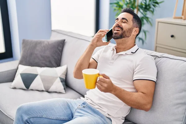Genç İspanyol adam kahve içiyor ve evde akıllı telefondan konuşuyor.