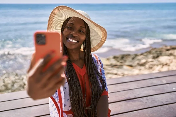Genç Afrikalı Amerikalı turist sahildeki bankta oturan akıllı telefonun yanında selfie çekiyor..
